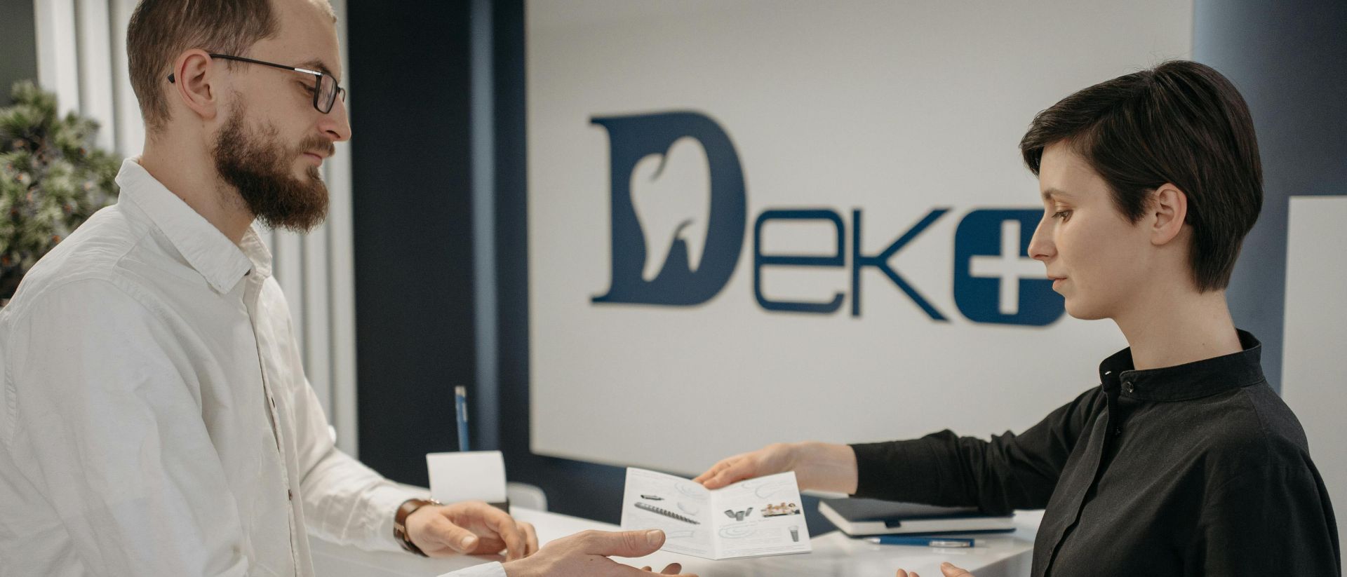 Man and woman exchanging paperwork at a modern dental clinic front desk.