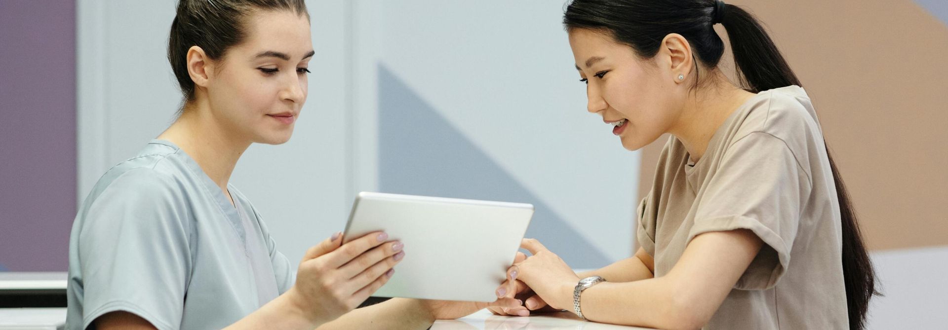 Two women interacting with a tablet at a modern reception desk indoors.