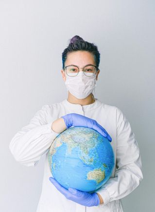 A medical professional wearing a mask and gloves holds a globe, symbolizing global health care during a pandemic.